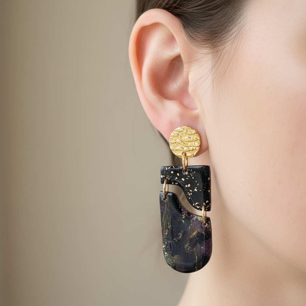 "Handmade polymer clay drop earrings with gold textured circular stud posts, black rectangular wavy cutout pieces and dark purple/black/gold mica shimmer elongated oval dangles"