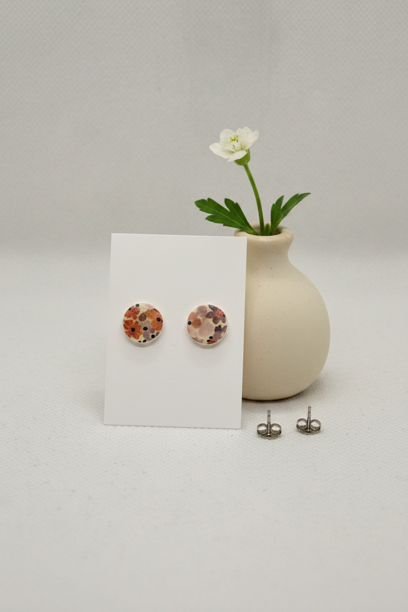 Handmade polymer clay Autumn Meadow circle stud earrings — Liberty-style floral print in warm rust, mauve and navy on cream, stainless steel posts, displayed on a white jewellery card propped against a ceramic vase