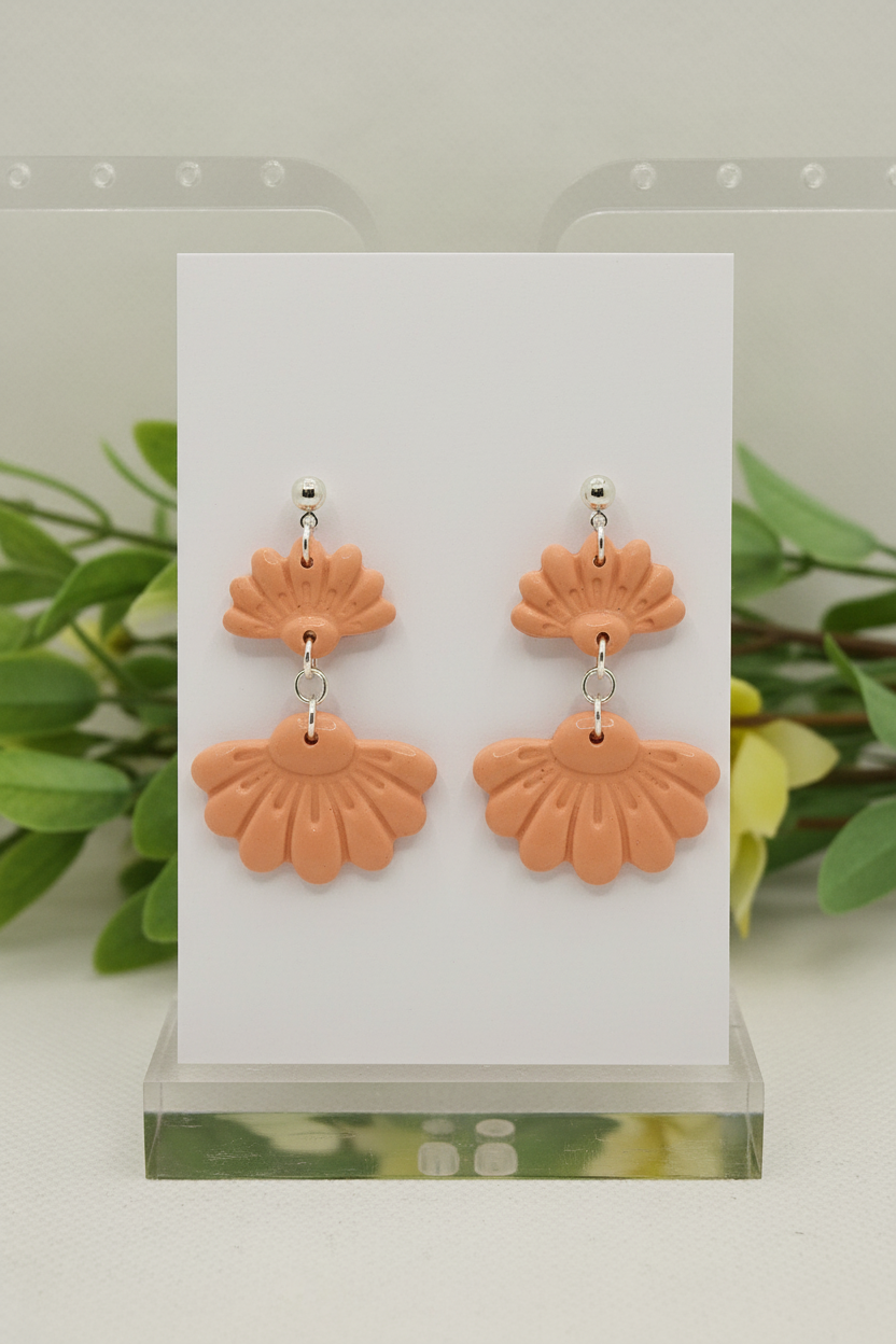 Handmade polymer clay Petal Tier Earrings in Brandied Melon — warm peachy-apricot two-tiered fan-shaped ruffled drops with silver ball stud, displayed on a plain white jewellery card with soft botanical background