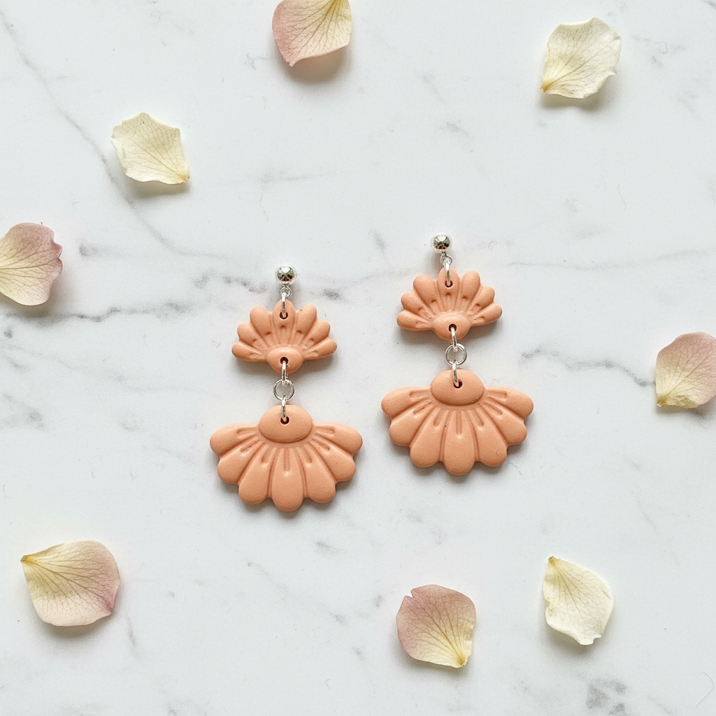 Flat lay of Crafty Larder Petal Tier Earrings in Brandied Melon on white marble with scattered petals — handmade polymer clay two-tiered fan-shaped ruffled drop earrings in warm peachy-apricot