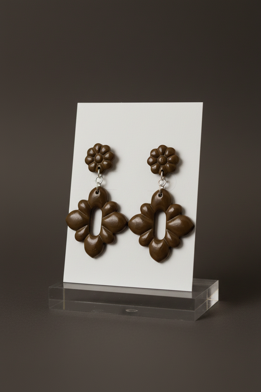 Handmade polymer clay Gerbera Drop Earrings in Bronze Brown — deep olive-brown gerbera flower stud top with quatrefoil drop, displayed on a plain white jewellery card on a clear acrylic stand
