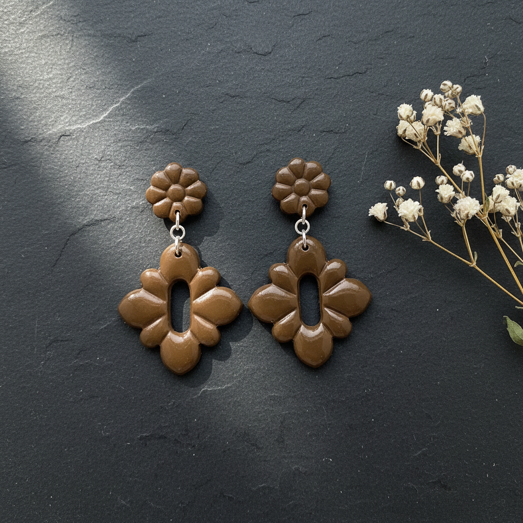 Flat lay of Crafty Larder Gerbera Drop Earrings in Bronze Brown on a dark moody surface with dried botanicals — handmade polymer clay dangle earrings in deep olive-brown