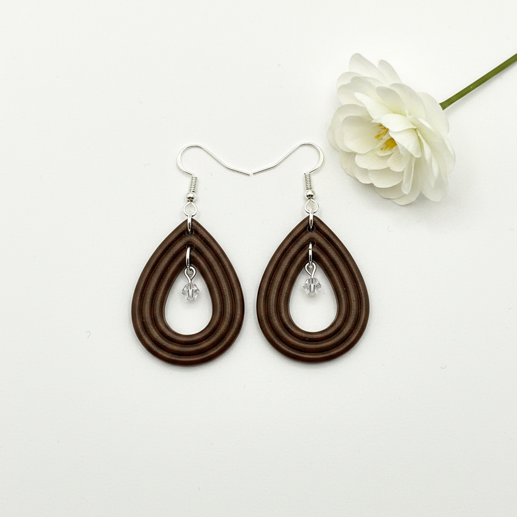 Overhead flat lay of Crafty Larder Raindrop Crystal Earrings in Bronze Brown on white surface with fresh flower — handmade polymer clay open teardrop hoop earrings with crystal bead drop in deep dark espresso brown