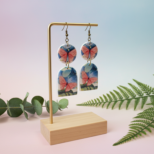 "Pink butterfly polymer clay earrings with blue watercolor background and brass arch connectors"