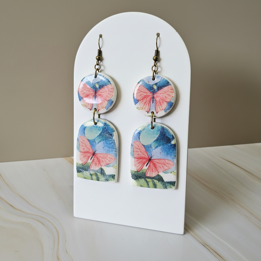 "Pink butterfly polymer clay earrings with blue watercolor background and brass arch connectors"