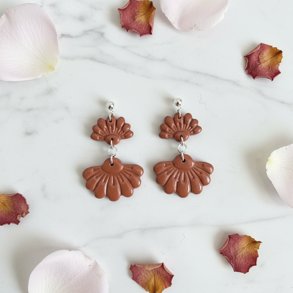 Flat lay of Crafty Larder Petal Tier Earrings in Chili Oil on white marble with scattered petals — handmade polymer clay two-tiered ruffled drop earrings in warm terracotta brown