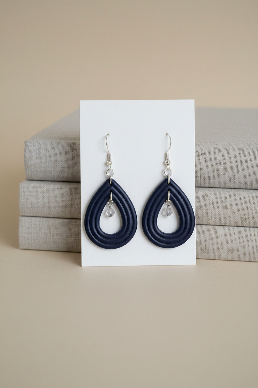 Handmade polymer clay Raindrop Crystal Earrings in Crown Blue — deep midnight navy open teardrop hoop earrings with crystal bead drop, displayed on a plain white jewellery card propped against linen