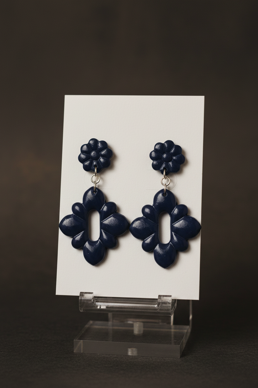 Handmade polymer clay Gerbera Drop Earrings in Crown Blue — deep midnight navy gerbera flower stud top with quatrefoil drop, displayed on a plain white jewellery card on a clear acrylic stand