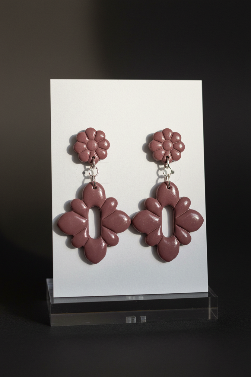 Handmade polymer clay Gerbera Drop Earrings in Damson — muted dusty plum gerbera flower stud top with quatrefoil drop, displayed on a plain white jewellery card on a clear acrylic stand