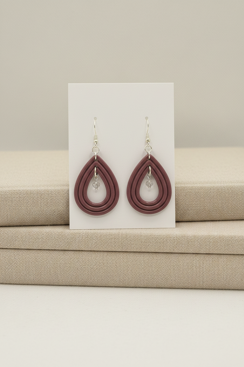 Handmade polymer clay Raindrop Crystal Earrings in Damson — muted dusty plum-mauve open teardrop hoop earrings with crystal bead drop, displayed on a plain white jewellery card propped against linen