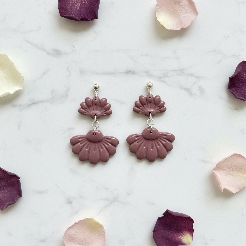 Flat lay of Crafty Larder Petal Tier Earrings in Damson on white marble with scattered petals — handmade polymer clay two-tiered ruffled drop earrings in muted dusty plum