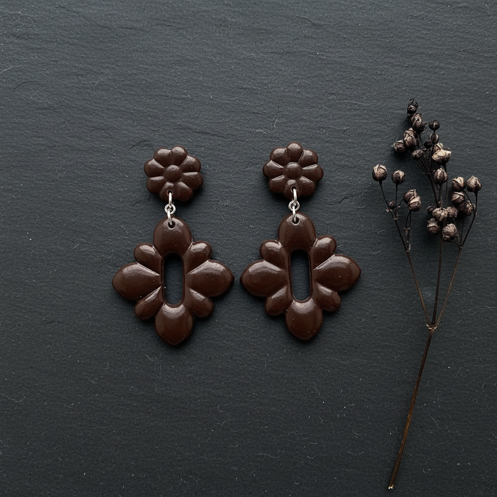 Flat lay of Crafty Larder Gerbera Drop Earrings in French Roast on a dark moody surface with dried botanicals — handmade polymer clay dangle earrings in deep espresso brown