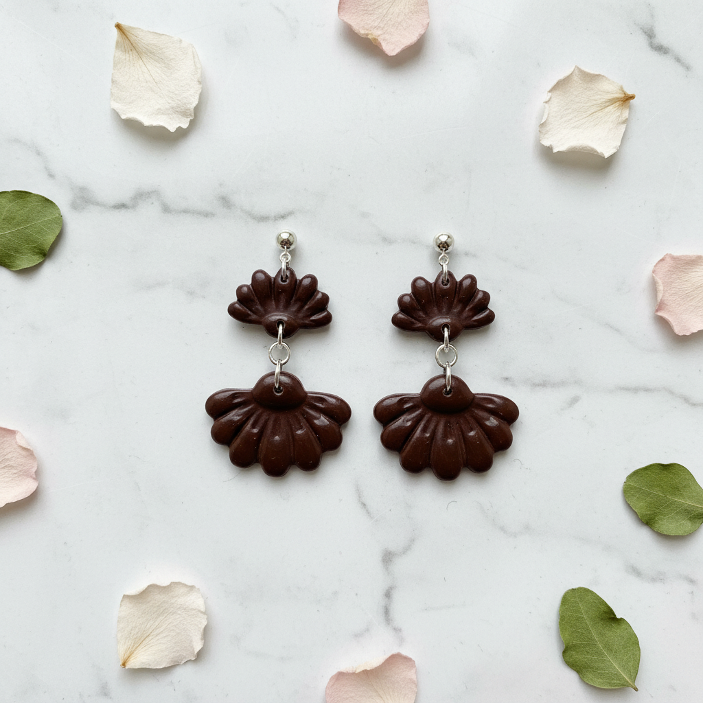 Flat lay of Crafty Larder Petal Tier Earrings in Hot Chocolate on white marble with scattered petals — handmade polymer clay two-tiered ruffled drop earrings in deep dark chocolate brown