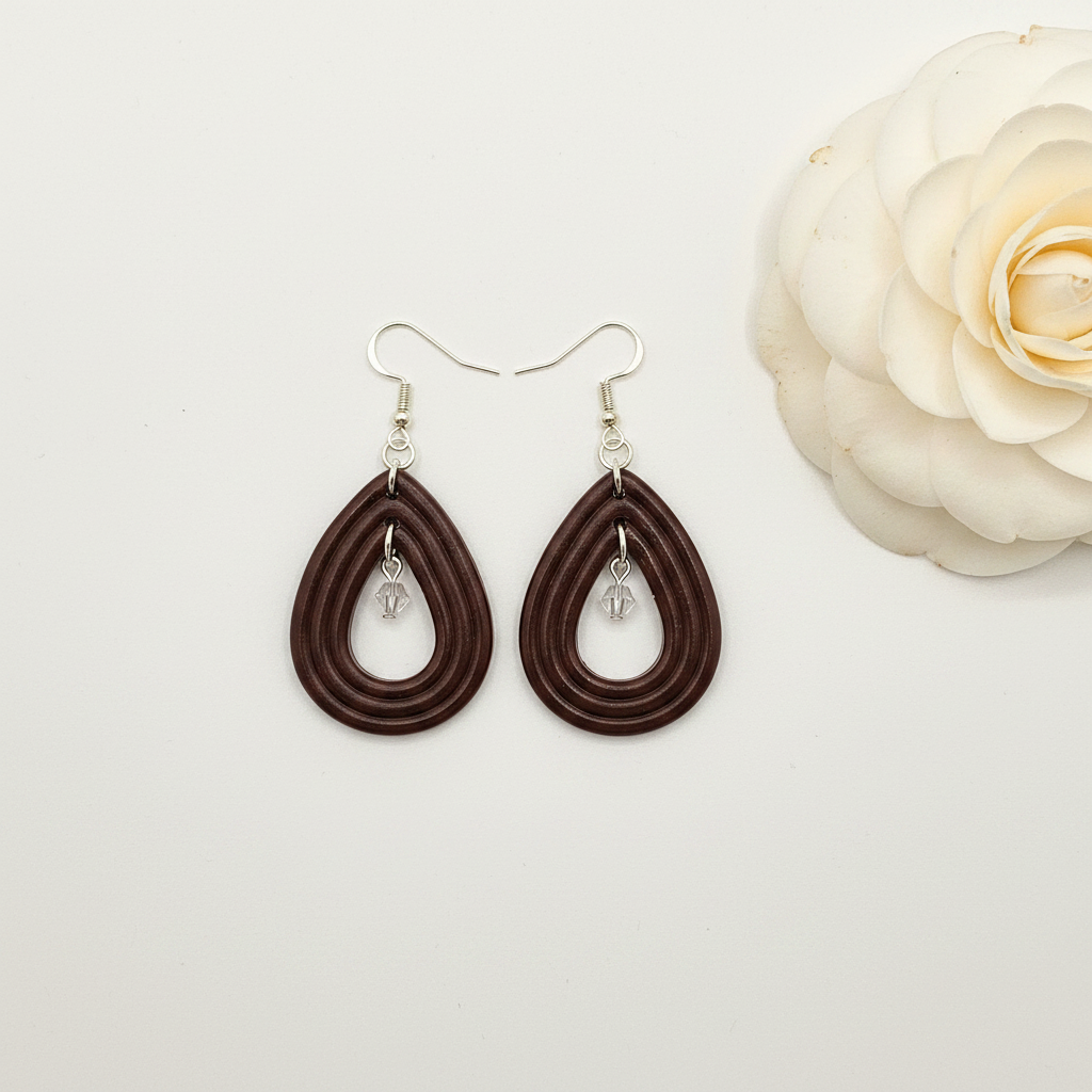 Overhead flat lay of Crafty Larder Raindrop Crystal Earrings in Hot Chocolate on white surface with fresh flower — handmade polymer clay open teardrop hoop earrings with crystal bead drop in deep dark chocolate brown