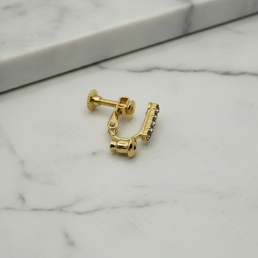 18k gold plated clip-on converter for stud earrings with crystal rhinestone bar, shown on its side on soft grey marble surface — Crafty Larder