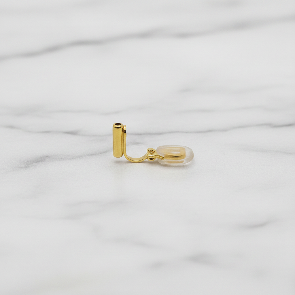 Close-up of a single 18k gold plated clip-on converter for French hook earrings, showing L-shaped gold bar with clear silicone comfort pad, on a soft grey marble surface — Crafty Larder