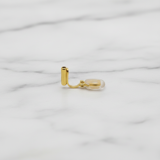 Close-up of a single 18k gold plated clip-on converter for French hook earrings, showing L-shaped gold bar with clear silicone comfort pad, on a soft grey marble surface — Crafty Larder