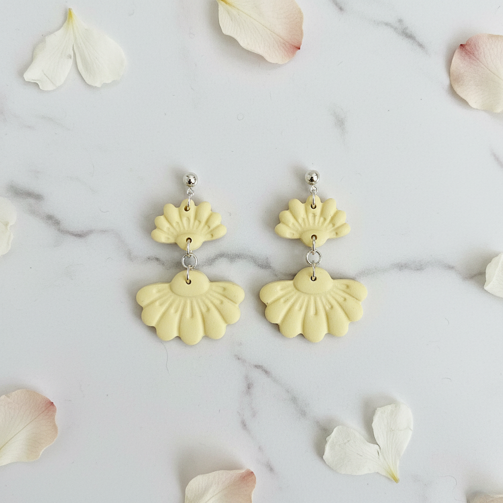 Flat lay of Crafty Larder Petal Tier Earrings in Lemon Grass on white marble with scattered petals — handmade polymer clay two-tiered fan-shaped ruffled drop earrings in soft butter yellow
