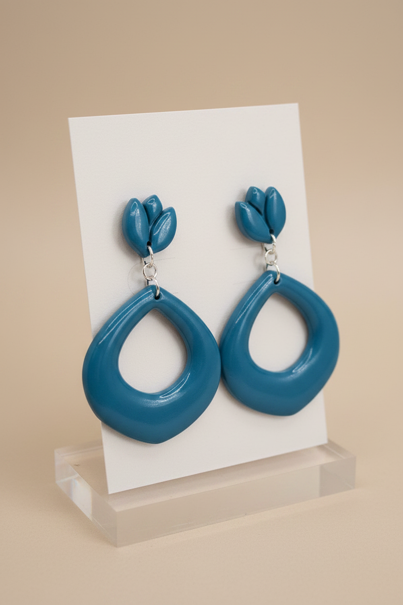 Handmade polymer clay Tulip Loop Earrings in Lyons Blue — rich teal-blue tulip stud top with open teardrop hoop drop, displayed on a plain white jewellery card on a clear acrylic stand