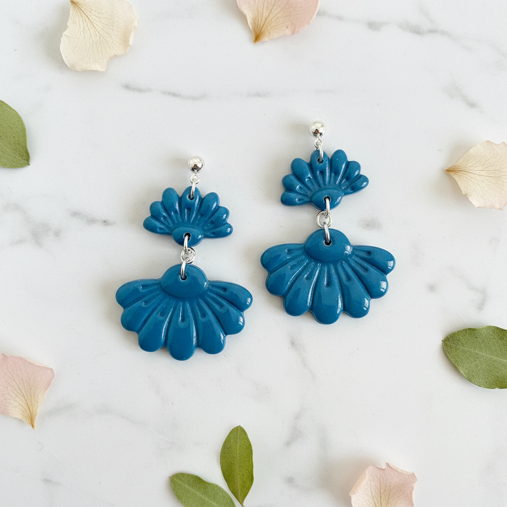 Flat lay of Crafty Larder Petal Tier Earrings in Lyons Blue on white marble with scattered petals — handmade polymer clay two-tiered fan-shaped ruffled drop earrings in teal-blue
