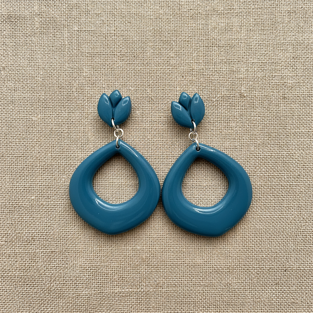 Flat lay of Crafty Larder Tulip Loop Earrings in Lyons Blue on a natural linen surface — handmade polymer clay dangle earrings in rich teal-blue