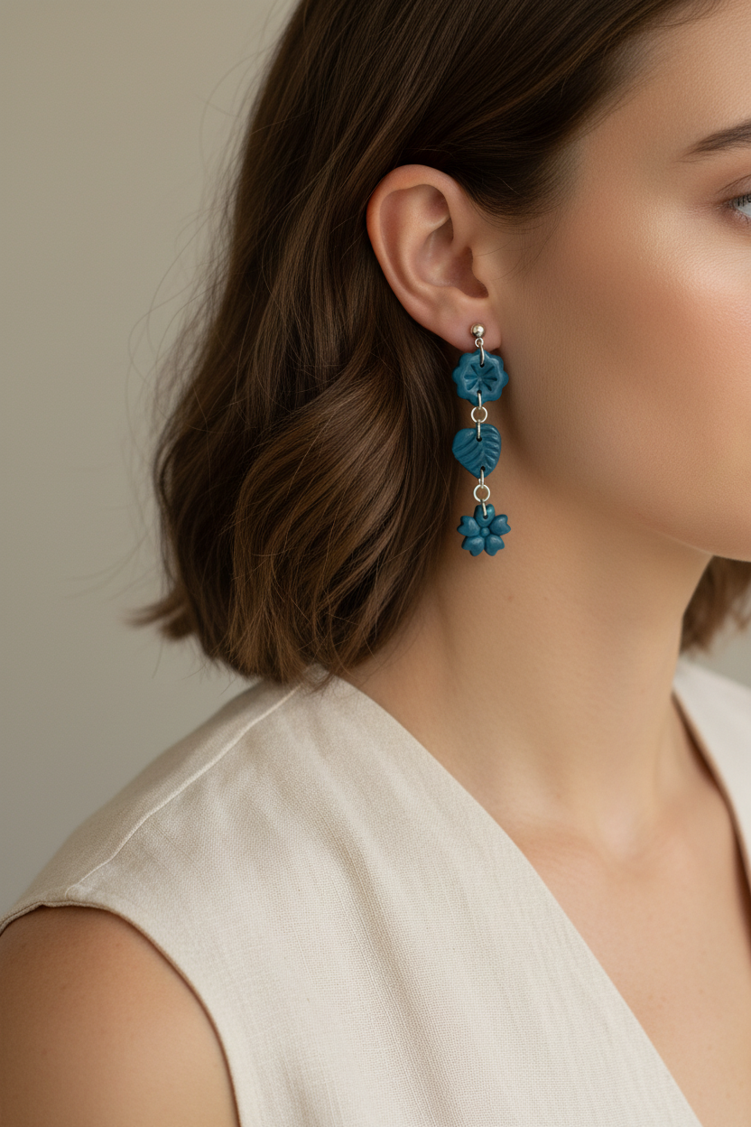 Model wearing Crafty Larder Botanical Trio Earrings in Lyons Blue — handmade polymer clay three-tier botanical drop earrings in rich teal-blue showing full length against neck and collarbone