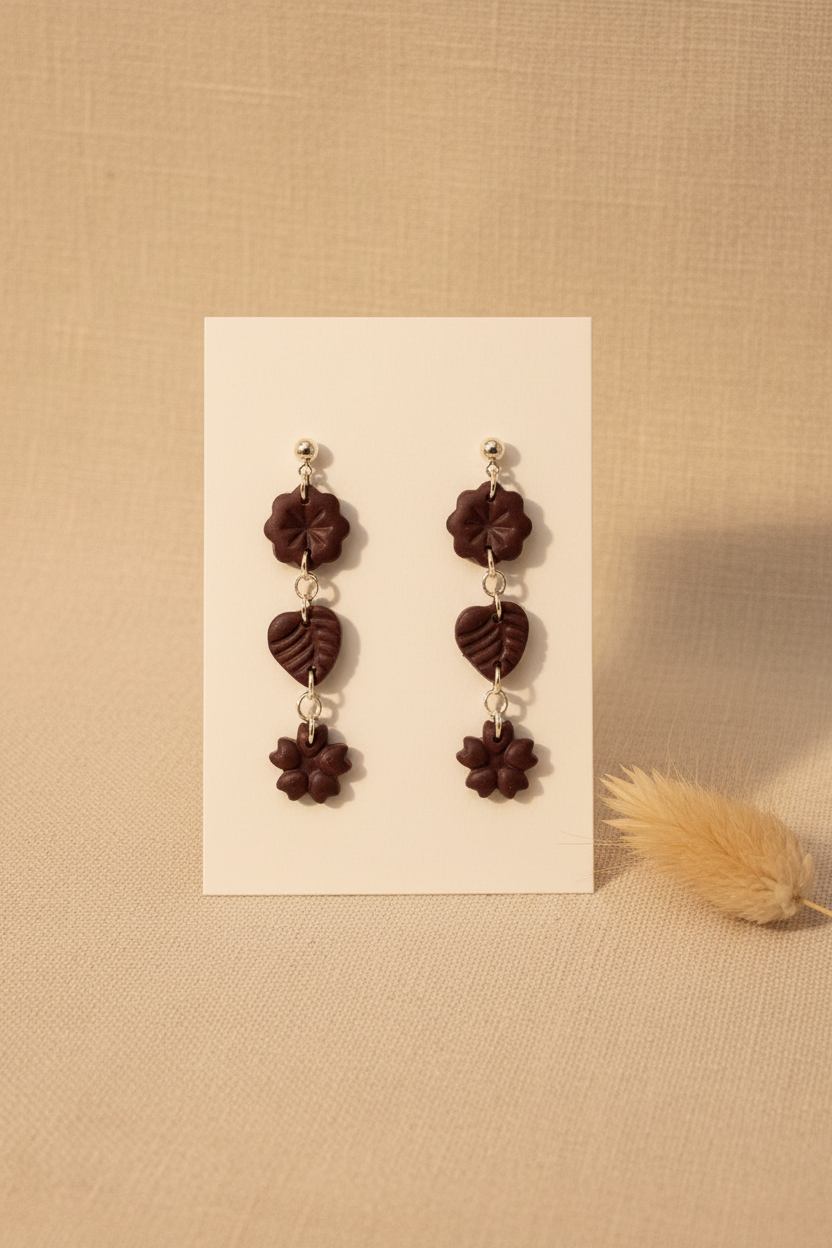 Handmade polymer clay Botanical Trio Earrings in Mauve Wine — deep burgundy three-tier flower, leaf & flower drop earrings on a plain white jewellery card with dried botanical stem