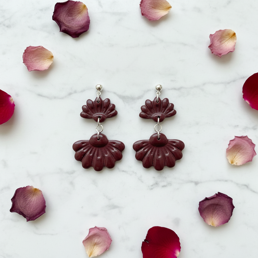 Flat lay of Crafty Larder Petal Tier Earrings in Mauve Wine on white marble with scattered petals — handmade polymer clay two-tiered ruffled drop earrings in deep burgundy