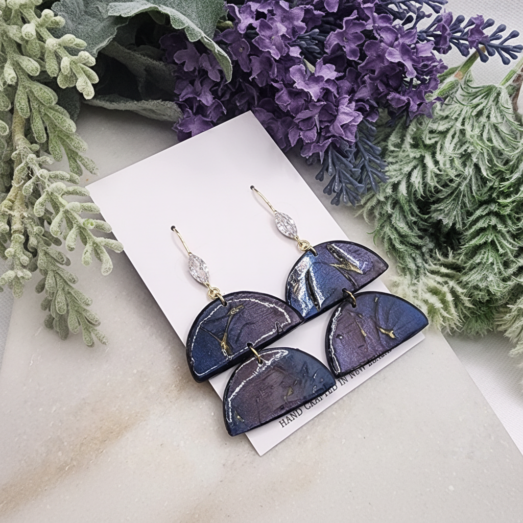"Handmade polymer clay two-tier half-moon earrings with gold shepherd hook ear wires featuring integrated cubic zirconia decoration and purple/blue mica shimmer half-moons"
