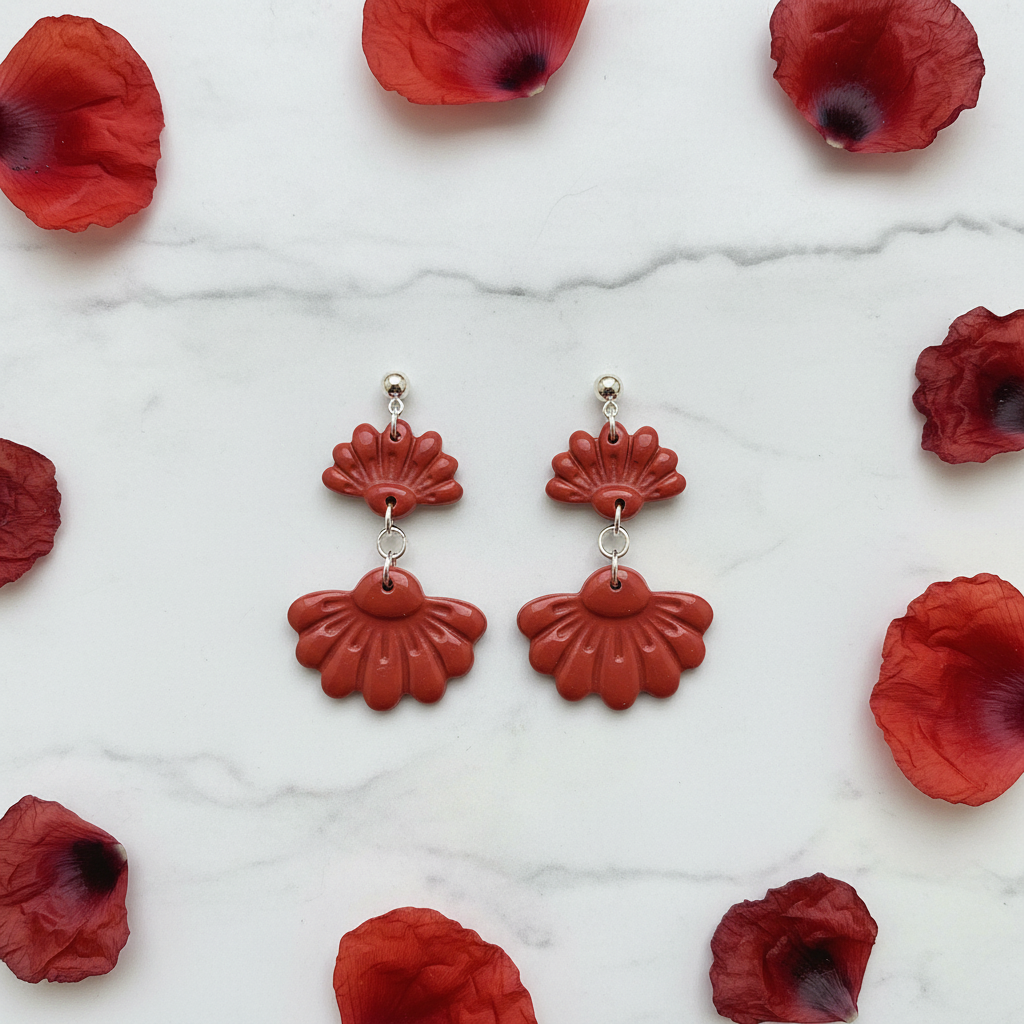 Flat lay of Crafty Larder Petal Tier Earrings in Poppy Red on white marble with scattered petals — handmade polymer clay two-tiered ruffled drop earrings in warm brick red