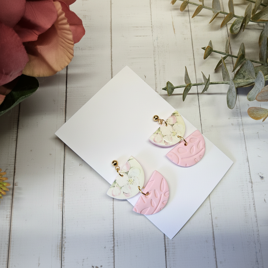  "Handmade polymer clay offset round earrings with cream/green floral half-circles and embossed pink half-circles in playful asymmetric arrangement"