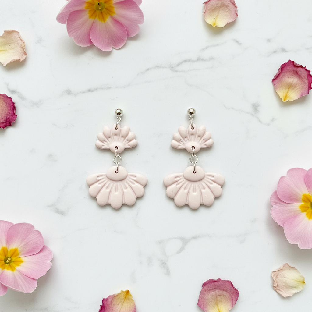 Flat lay of Crafty Larder Petal Tier Earrings in Primrose Pink on white marble with scattered petals — handmade polymer clay two-tiered fan-shaped ruffled drop earrings in soft pale blush