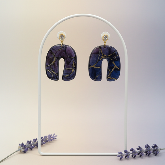 "Handmade polymer clay U-shaped arch earrings with gold textured teardrop stud posts and purple/blue mica shimmer dangles with gold marbling"