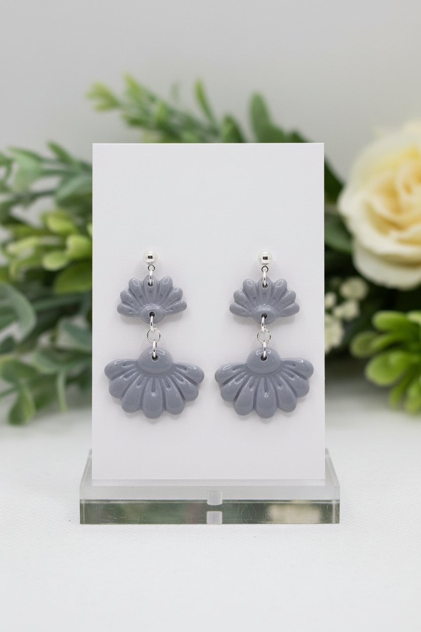 Handmade polymer clay Petal Tier Earrings in Vapor Blue — soft cool grey-blue two-tiered fan-shaped ruffled drops with silver ball stud, displayed on a plain white jewellery card with soft botanical background