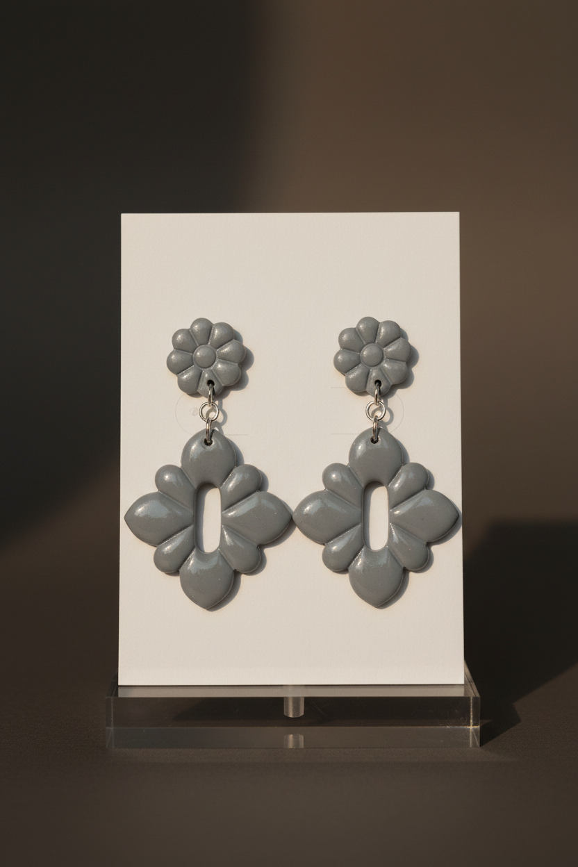Handmade polymer clay Gerbera Drop Earrings in Vapor Blue — soft cool grey-blue gerbera flower stud top with quatrefoil drop, displayed on a plain white jewellery card on a clear acrylic stand