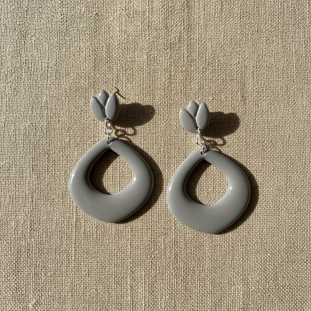 Flat lay of Crafty Larder Tulip Loop Earrings in Vapor Blue on a natural linen surface — handmade polymer clay dangle earrings in cool muted grey-blue