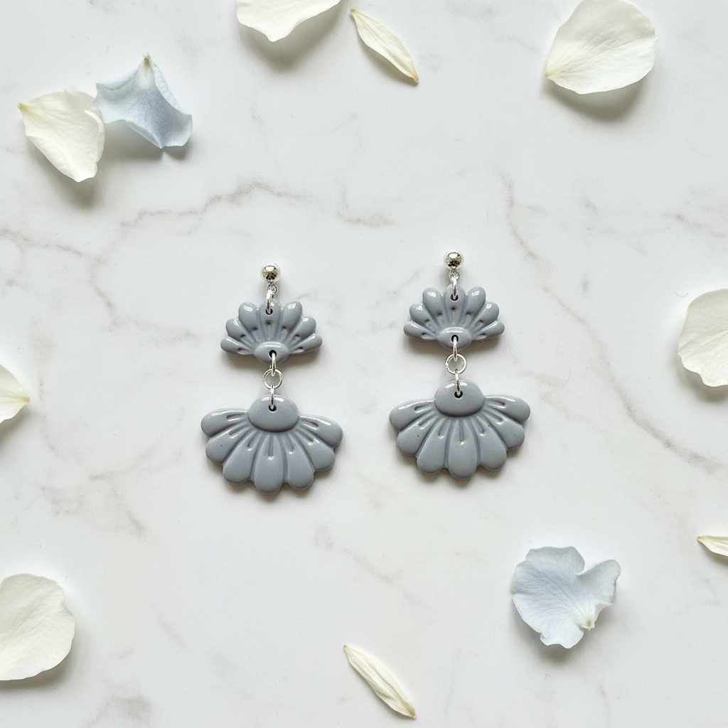 Flat lay of Crafty Larder Petal Tier Earrings in Vapor Blue on white marble with scattered petals — handmade polymer clay two-tiered fan-shaped ruffled drop earrings in soft cool grey-blue